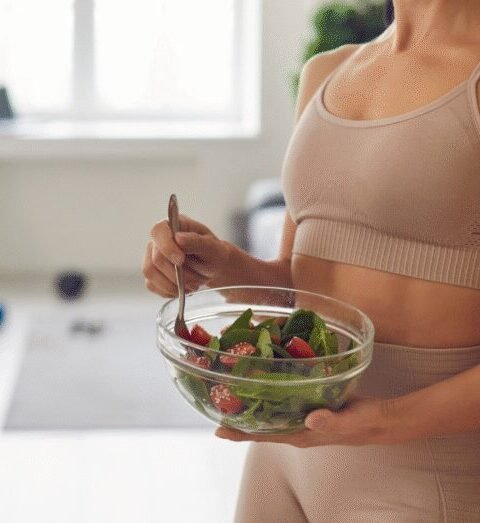 Woman holding a bowl of fresh vegetables and salad in a bright kitchen