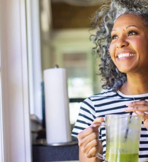 Woman smiling while holding a cup of tea near a window