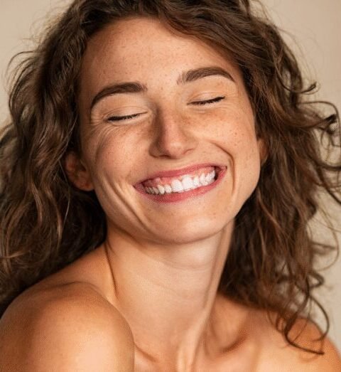 Woman smiling with her eyes closed against a neutral background